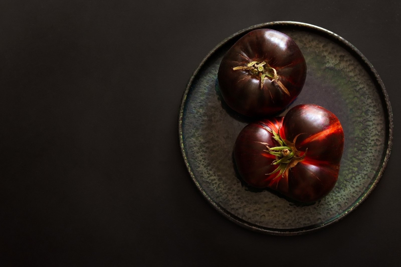Two dark red-brown tomatoes with green shoulders on a plate