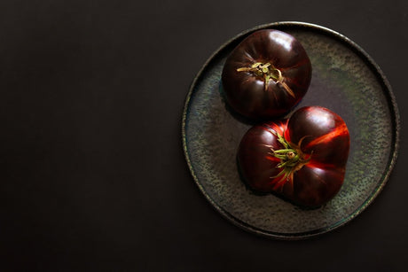 Two dark red-brown tomatoes with green shoulders on a plate