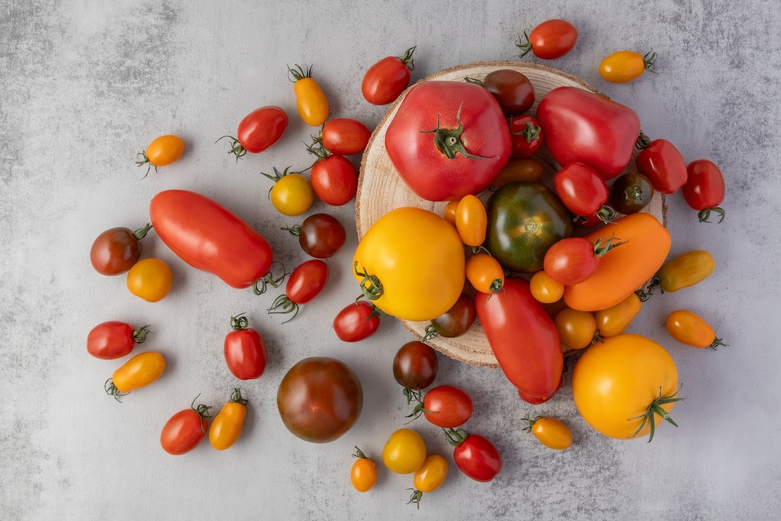 An overhead assortment of red, yellow, orange, and dark tomatoes in several sizes