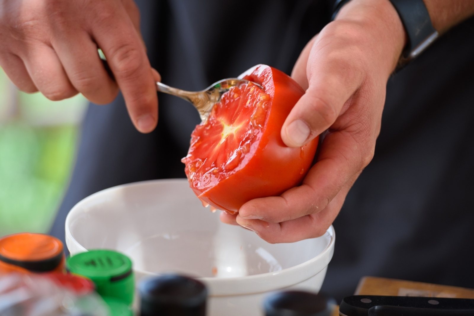 A spoon removing seed and gel from a cut tomato into a bowl