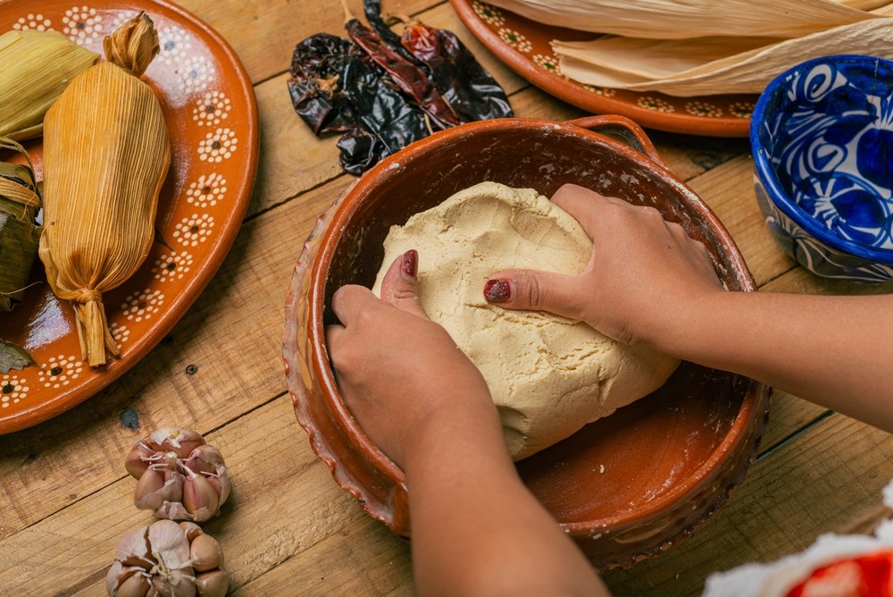 Hands kneading corn masa in a clay bowl