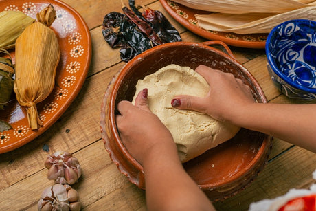 Hands kneading corn masa in a clay bowl