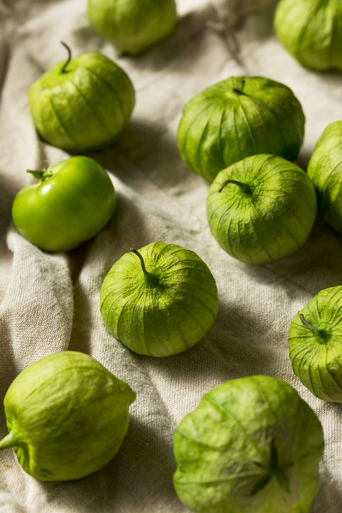 Green tomatillos in dry papery husks arranged on cloth