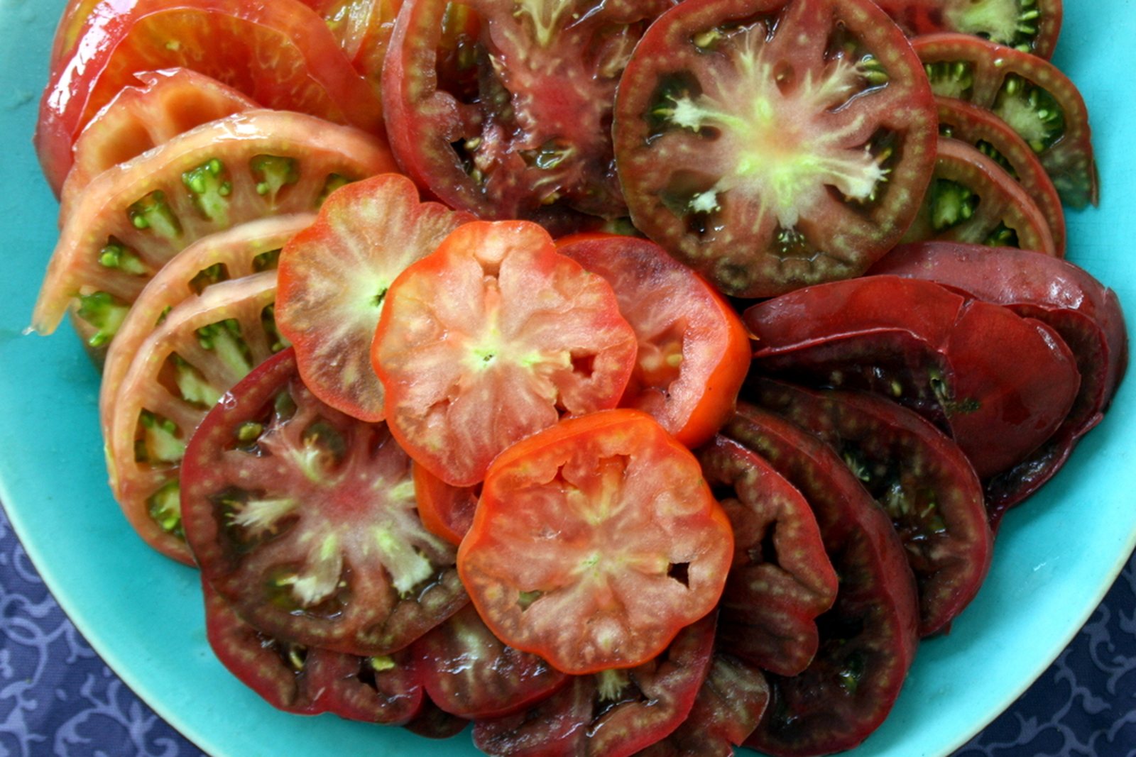 Sliced pink, red, and dark tomatoes showing flesh, gel, and seed cavities