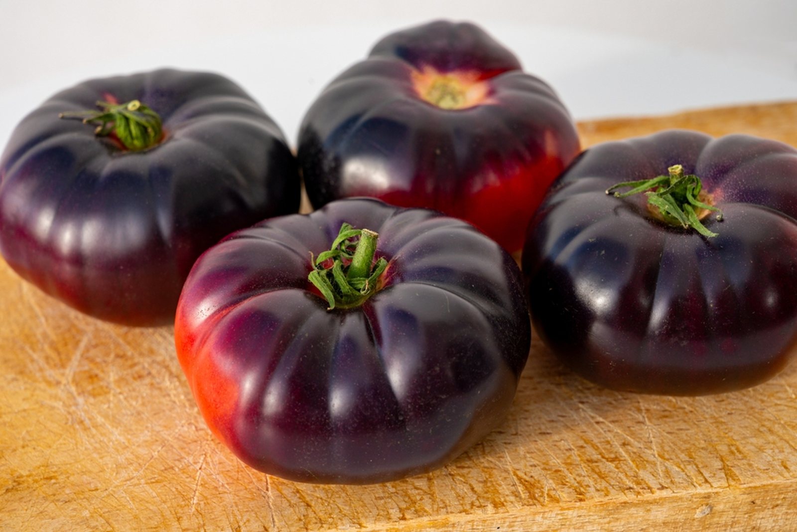 Several very dark purple ribbed tomatoes on a wooden surface