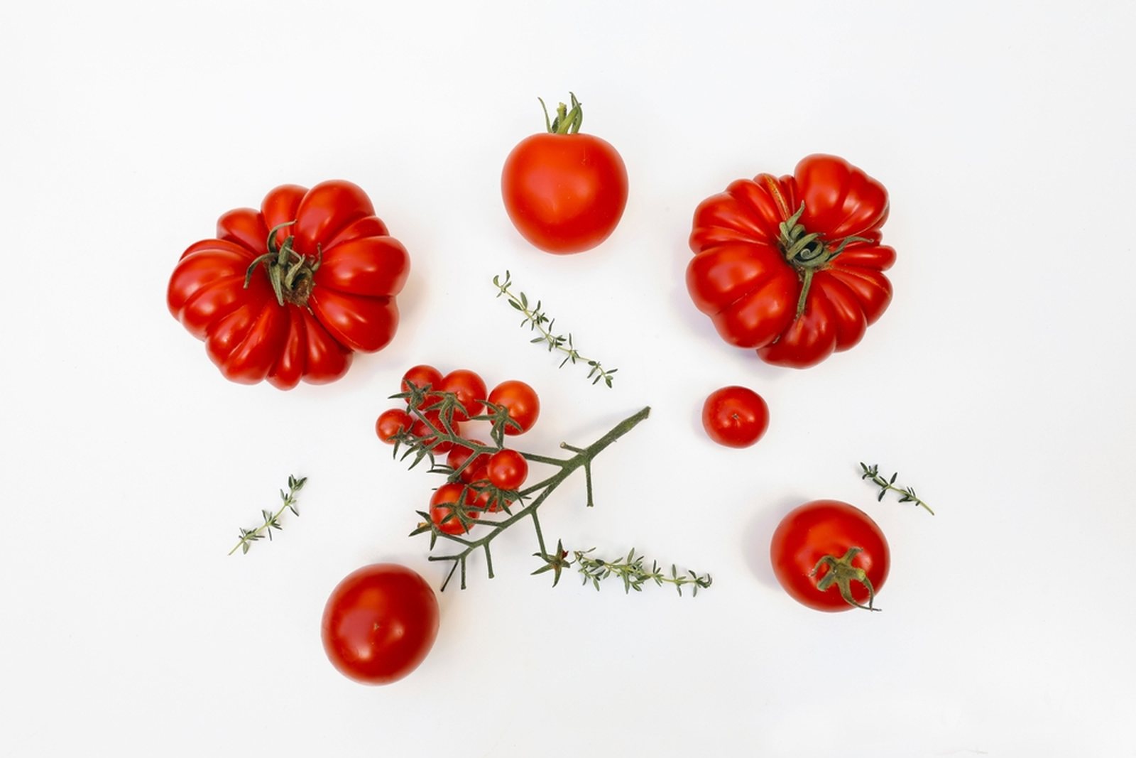 Ribbed, round, cherry, and small tomatoes arranged on a white background