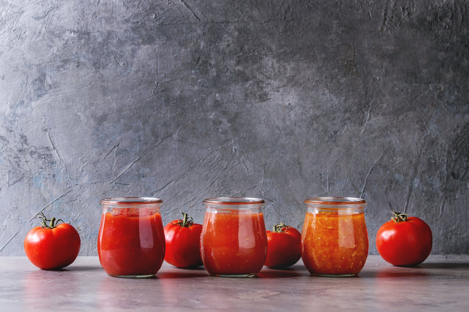 Three jars of tomato sauce beside whole red tomatoes