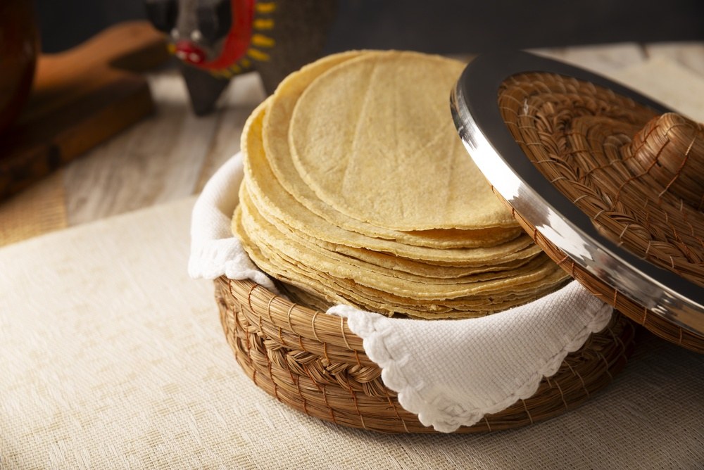 Stack of freshly made corn tortillas in a covered basket