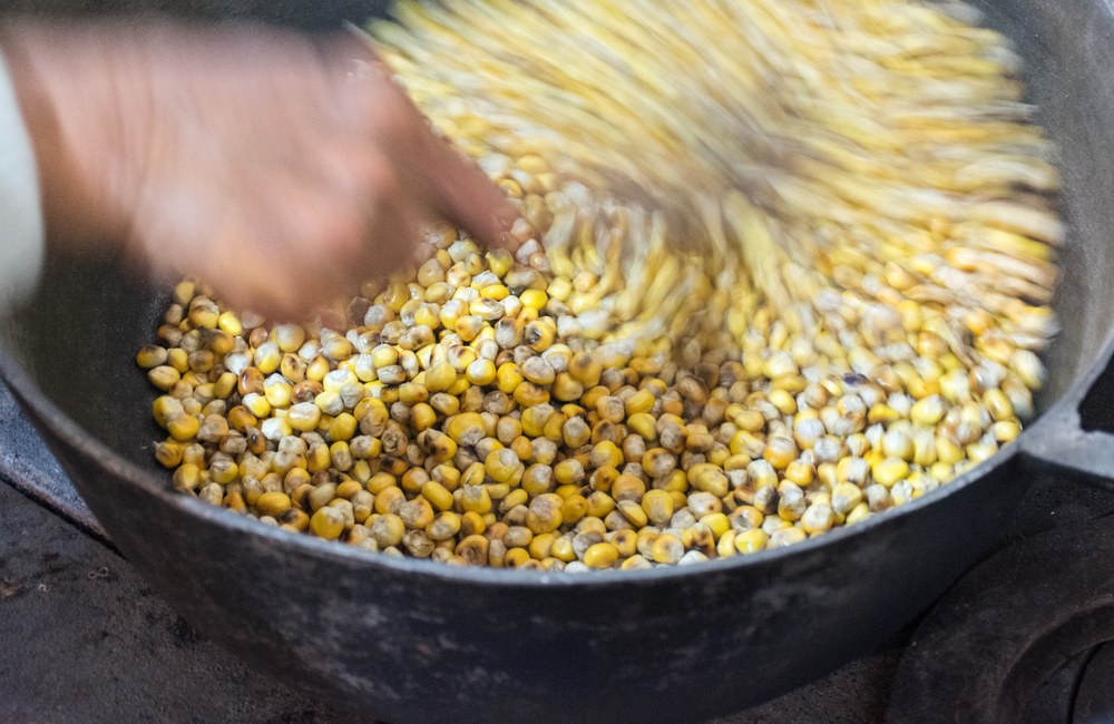Dry corn kernels being stirred in a heavy pot