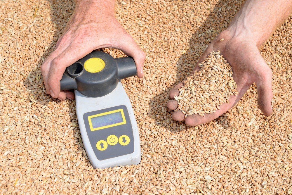 Handheld grain moisture meter beside a sample of dry grain