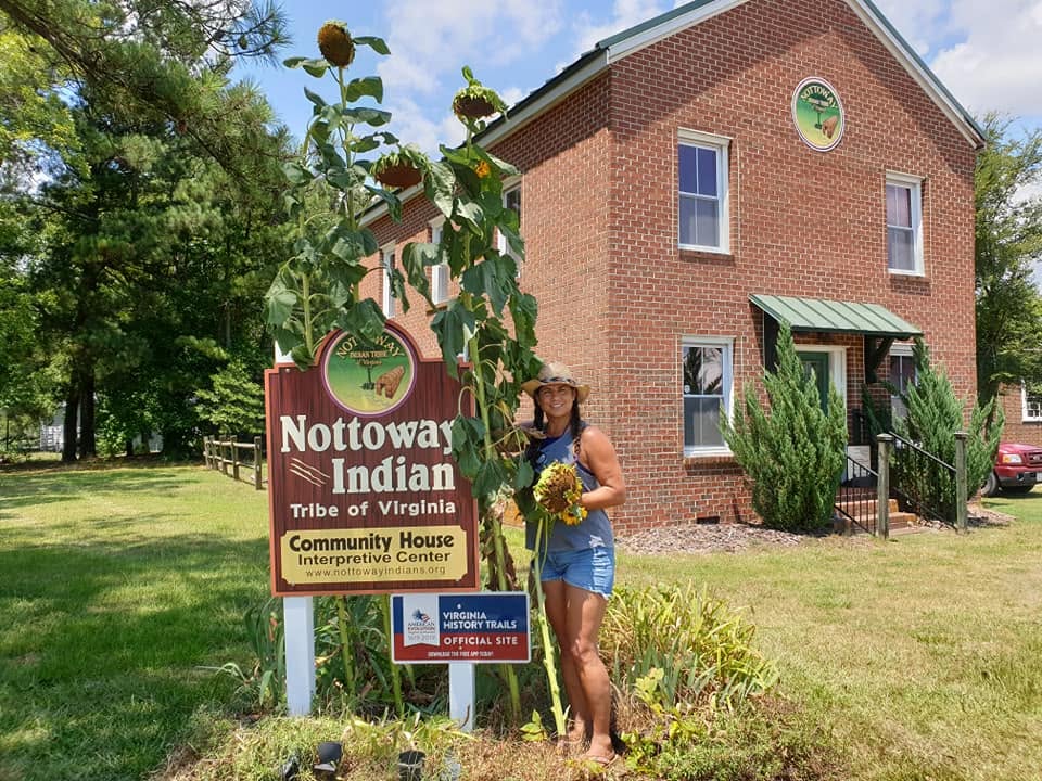 Elizabeth Roach Cain standing beside the Nottoway Indian Tribe of Virginia Community House sign